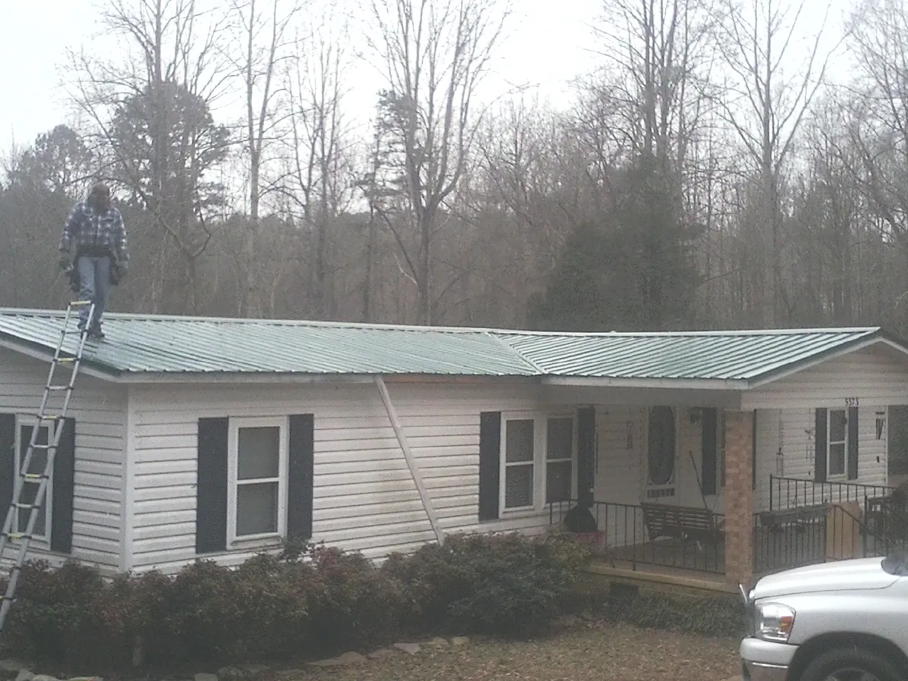 Worker on a ladder beside a new green metal roof on a ranch home in Reedsburg