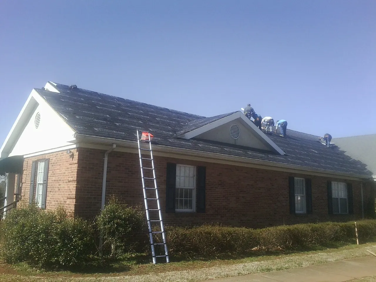 Crew tearing shingles off a brick ranch roof with a ladder set — Metal Roof Repair work by our crew in Reedsburg
