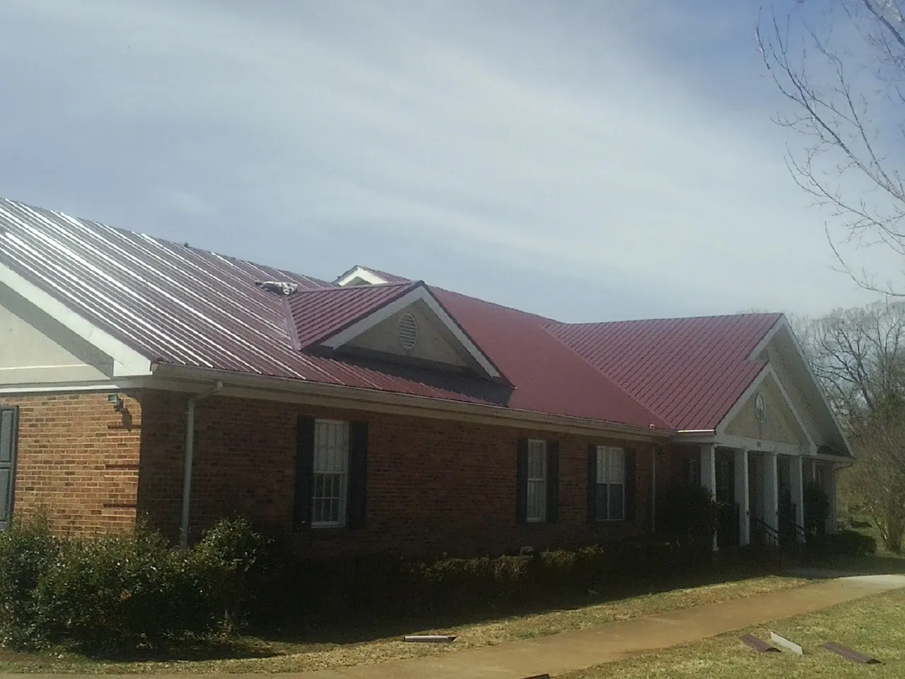 Red metal roof with gabled entries on a long brick building, from a Hail Damage Roof Repair job in Reedsburg