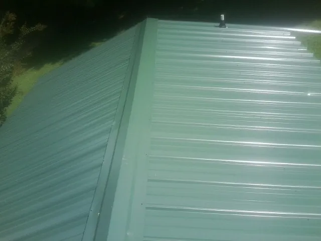 New green metal panels meeting at the ridge of a roof — Flat Roof Repair work by our crew in Reedsburg