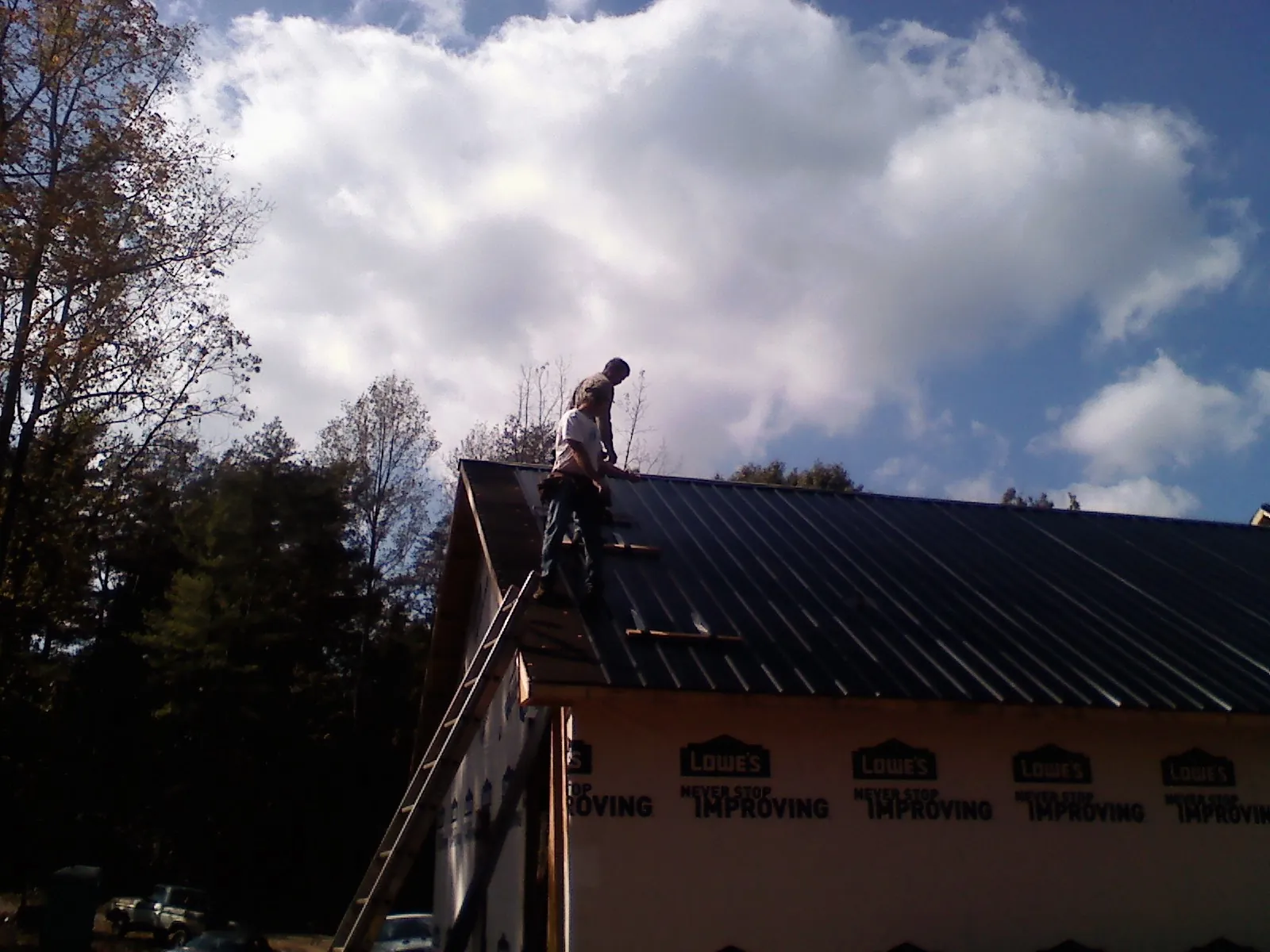 Roofer fastening dark metal panels high against a cloudy sky, from a Roof Inspection job in Reedsburg
