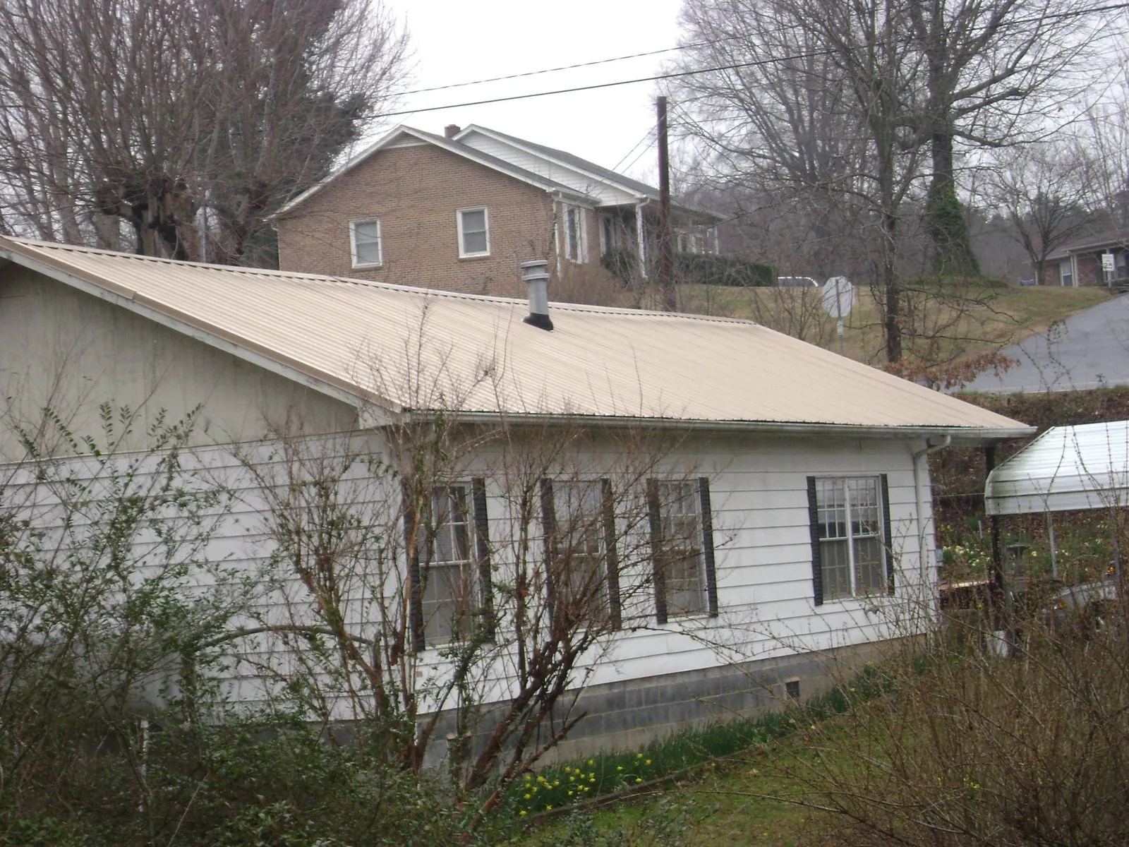 Tan metal roof on a white sided house set into a hillside — Commercial Roofing by Roofing Brothers in Reedsburg